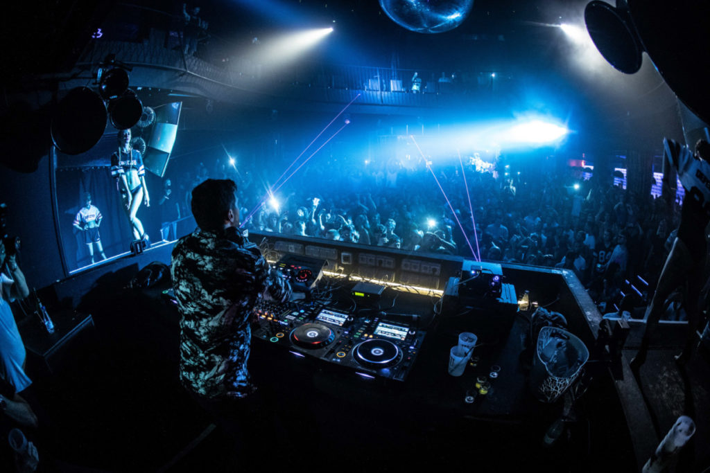 DJ working the decks in a dark, blue-lit club while the crowd dances — the booth stays clear of request interruptions